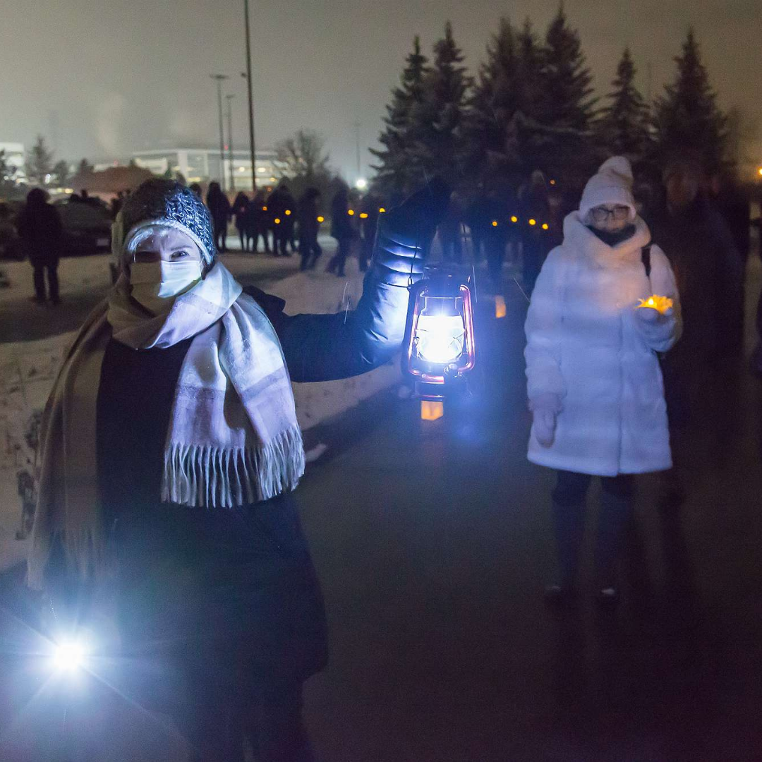 A woman with a lantern lights the way for others walking towards The Gies Family Centre.