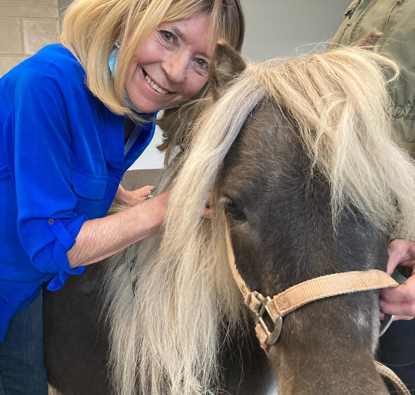 woman in blue shirt smiles while posing with a pony