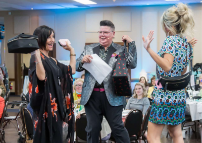 The Auctionista and two other women stand facing each other holding handbags and posing