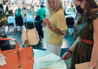 Two women are looking at an auction table with purses