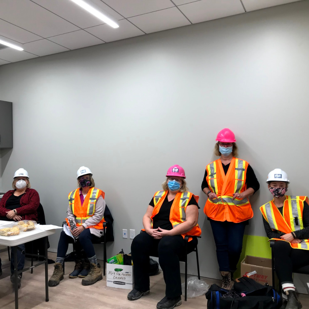 A group of HWR staff in orange vests and masks sit in the kitchen at The Gies Family Centre