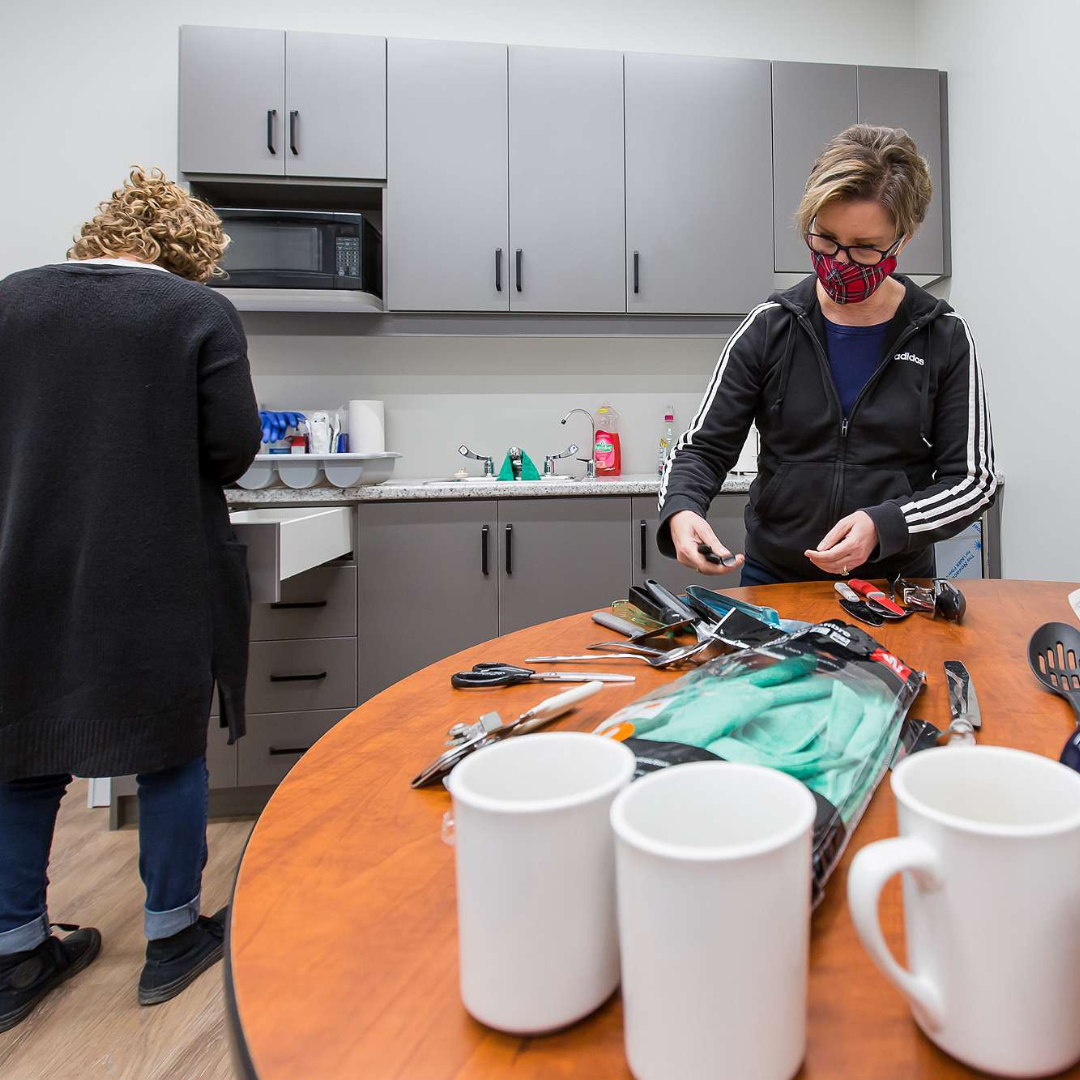 Two women unload cutlery and dishes in the kitchen at The Gies Family Centre