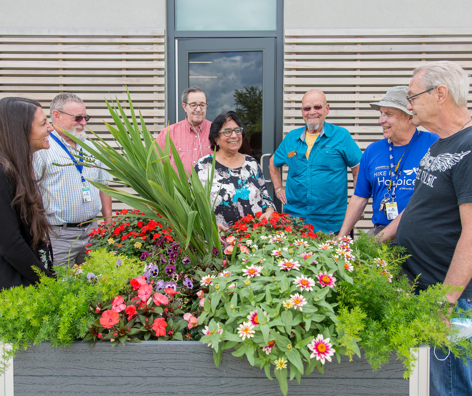 A group of men and women stand around a garden, laughing