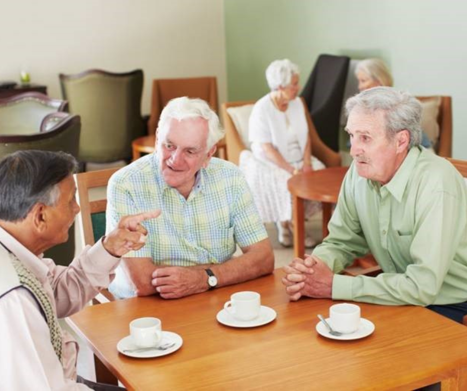 Three men sit at a table talking, and drinking coffee