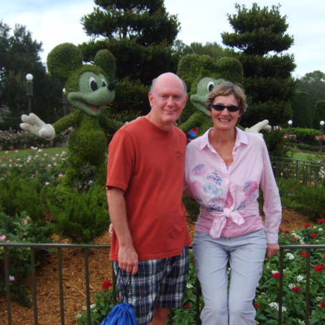 A man and woman pose for a photo in front of Mickey Mouse shrubbery.