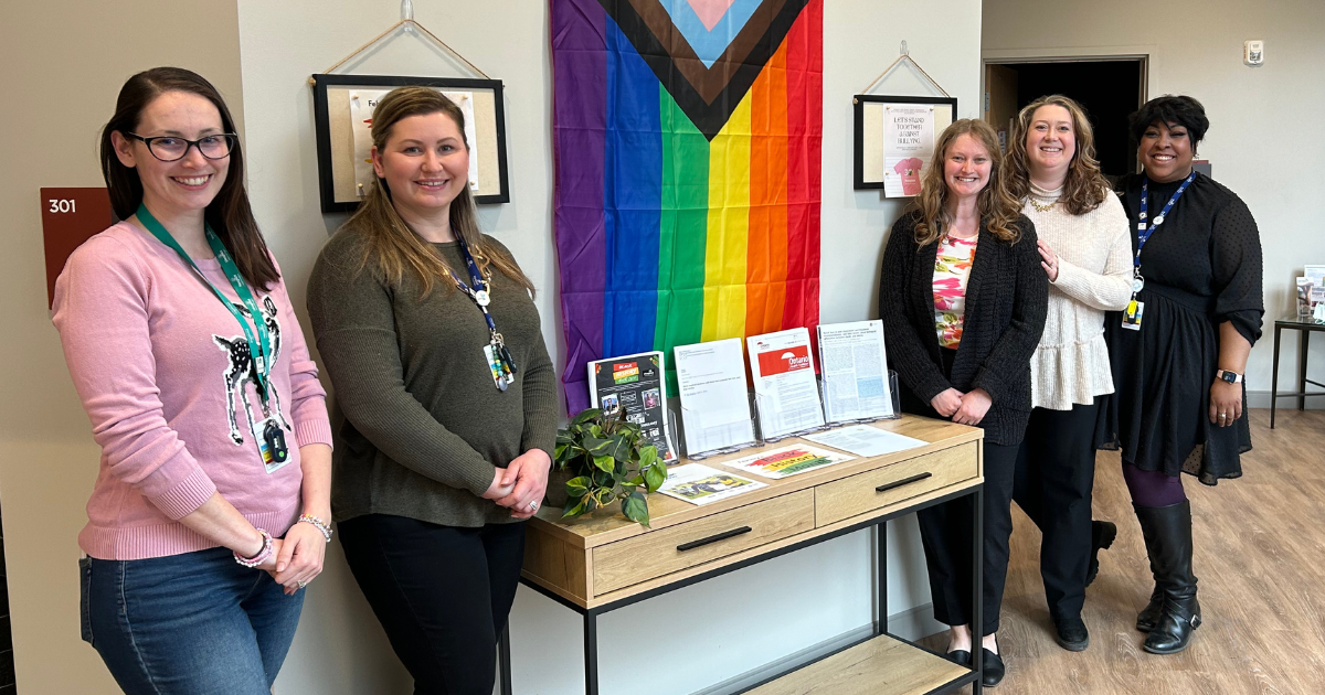 Photo of 5 women standing around a pride flag and a table to documents.